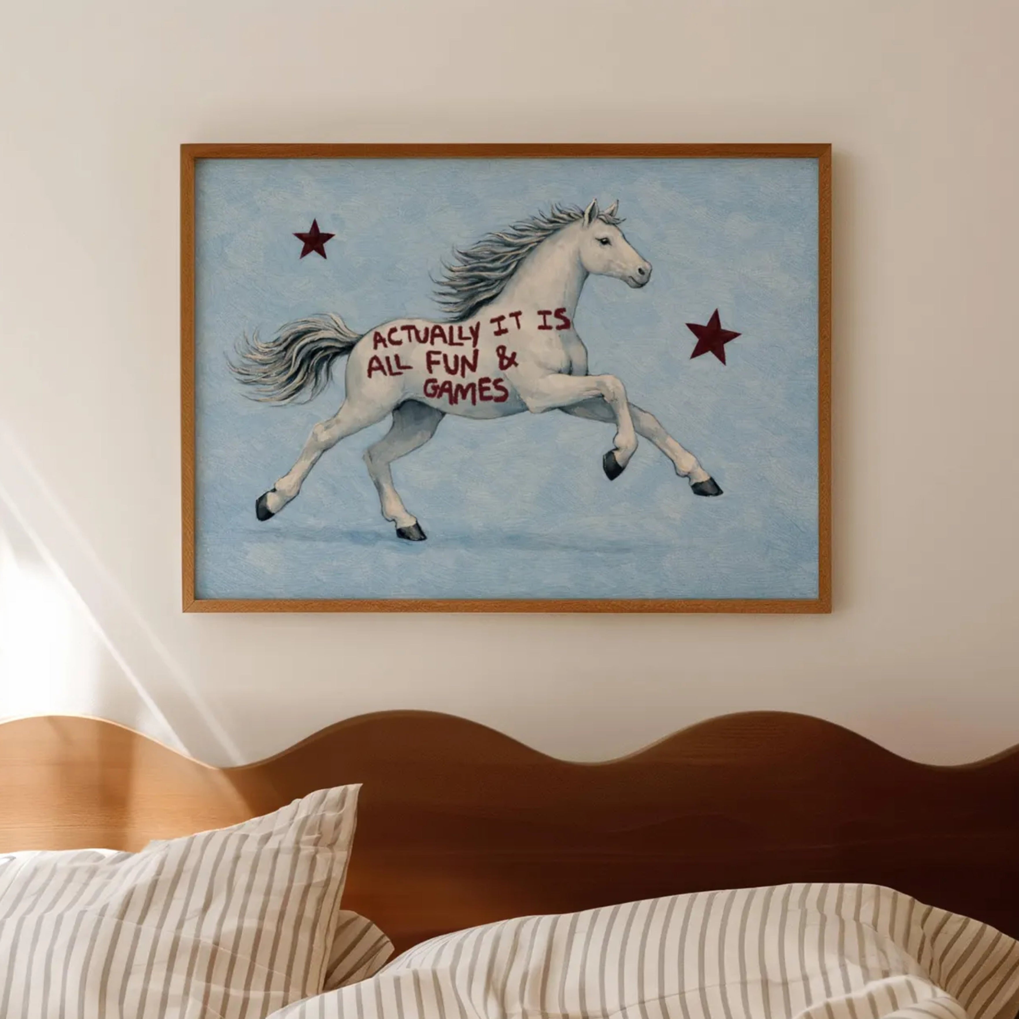 A surreal Symbolic artwork featuring a White Horse running against a pale blue background with Burgundy stars. The Horse has handwritten quote "Actually It Is All Fun and Games". This is a hand drawn Contemporary Folk art Print Oil Painting