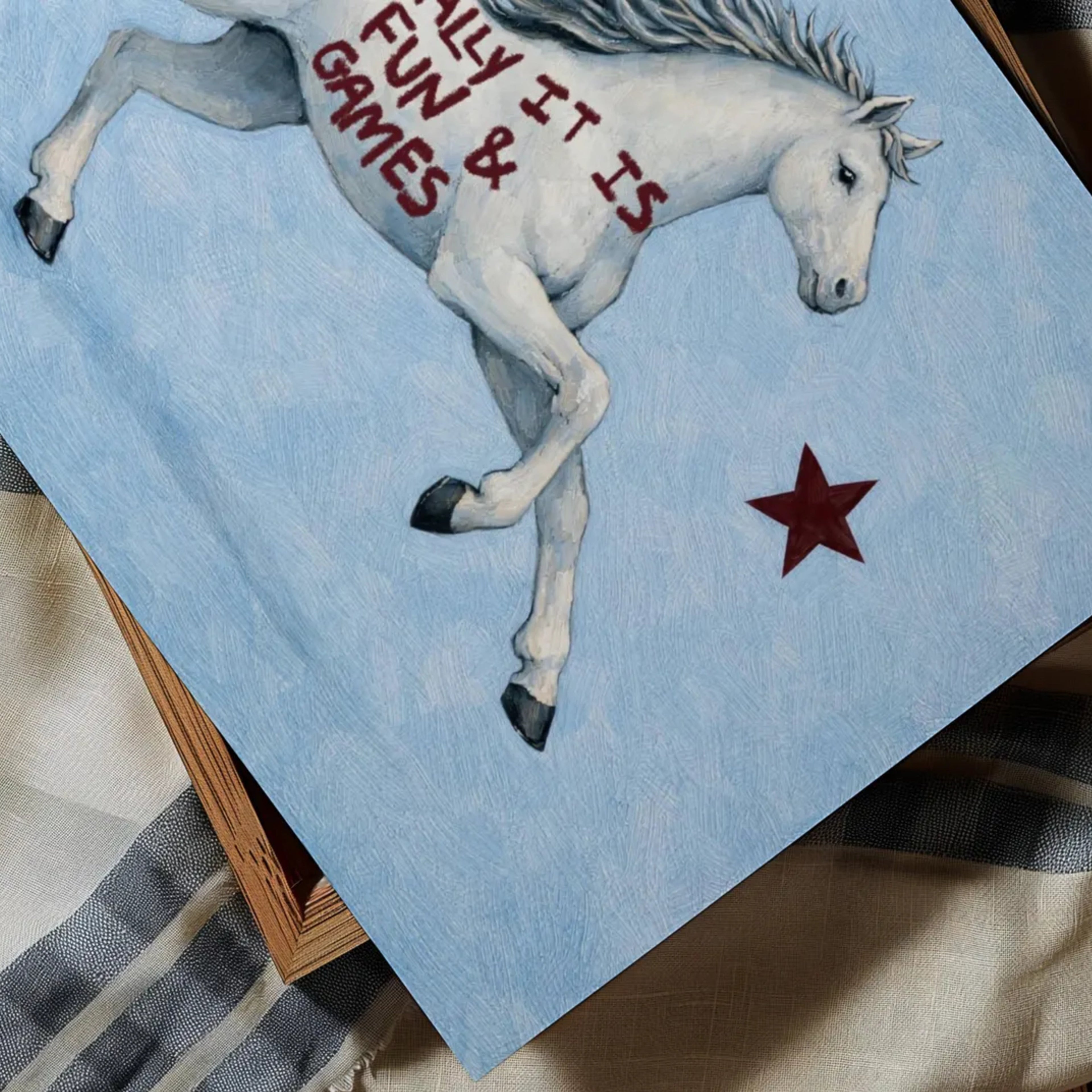 A surreal Symbolic artwork featuring a White Horse running against a pale blue background with Burgundy stars. The Horse has handwritten quote "Actually It Is All Fun and Games". This is a hand drawn Contemporary Folk art Print Oil Painting.