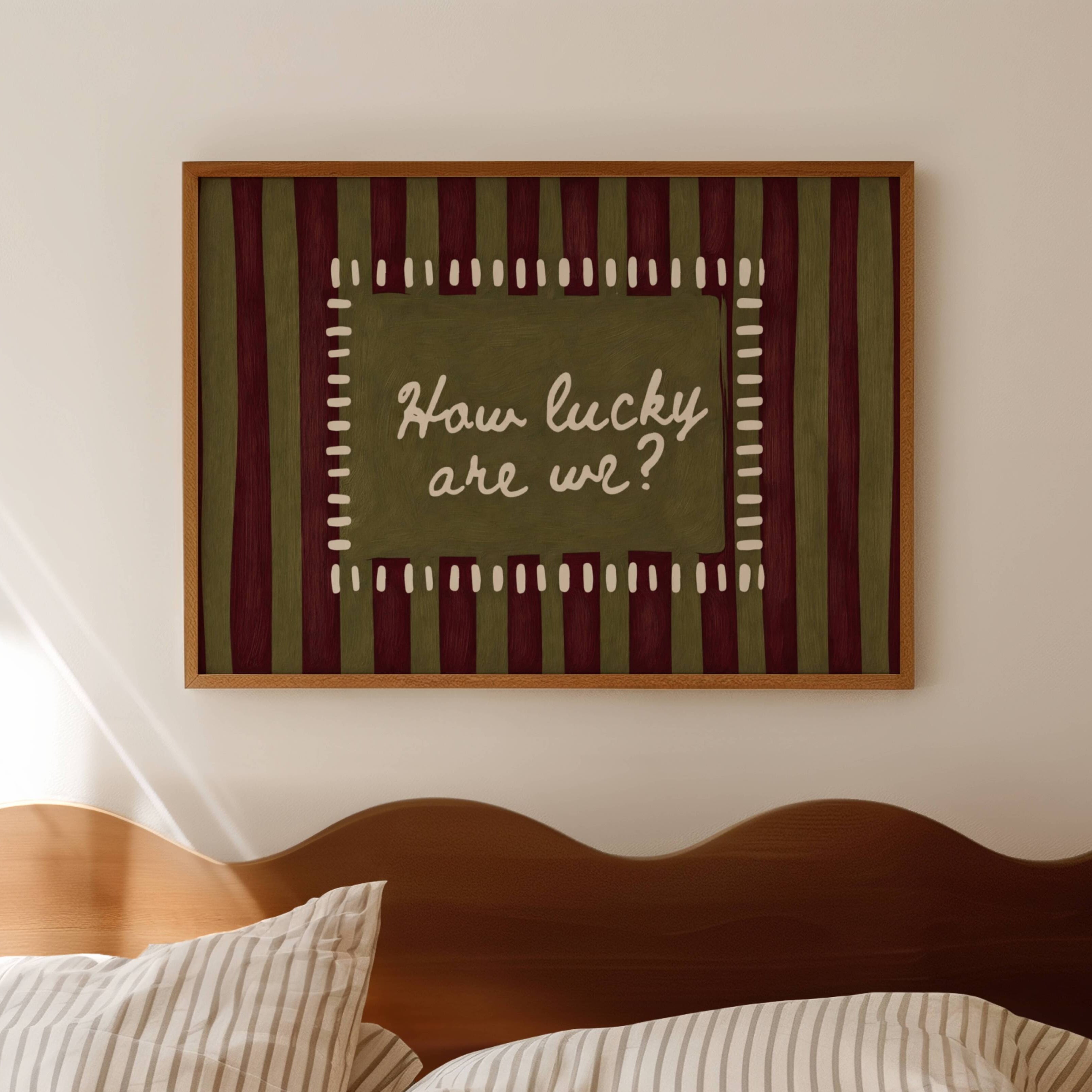 hand drawn Playful typography print with the phrase "How Lucky Are We?" on a khaki and ruby burgundy striped background. This is a hand drawn trendy typography wall art print ideal for bedrooms, dorm room decor, gallery walls and playful interiors.