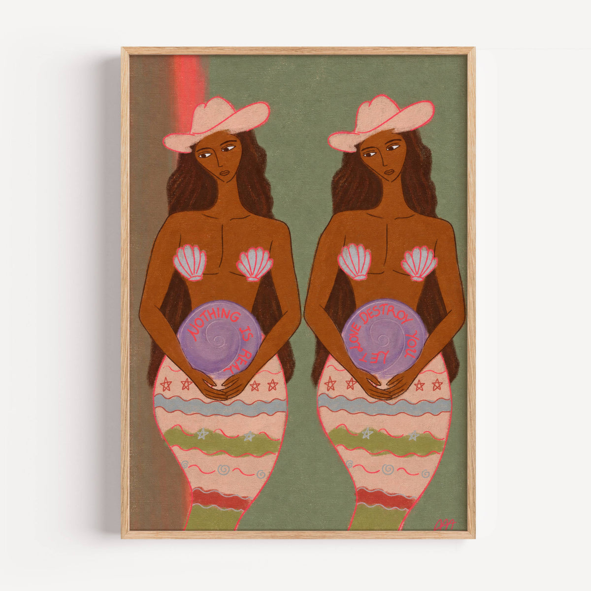 A framed art print featuring a stylized illustration of two mermaid women with pink hats and seashell tops, set against a muted green background with a light wood frame.