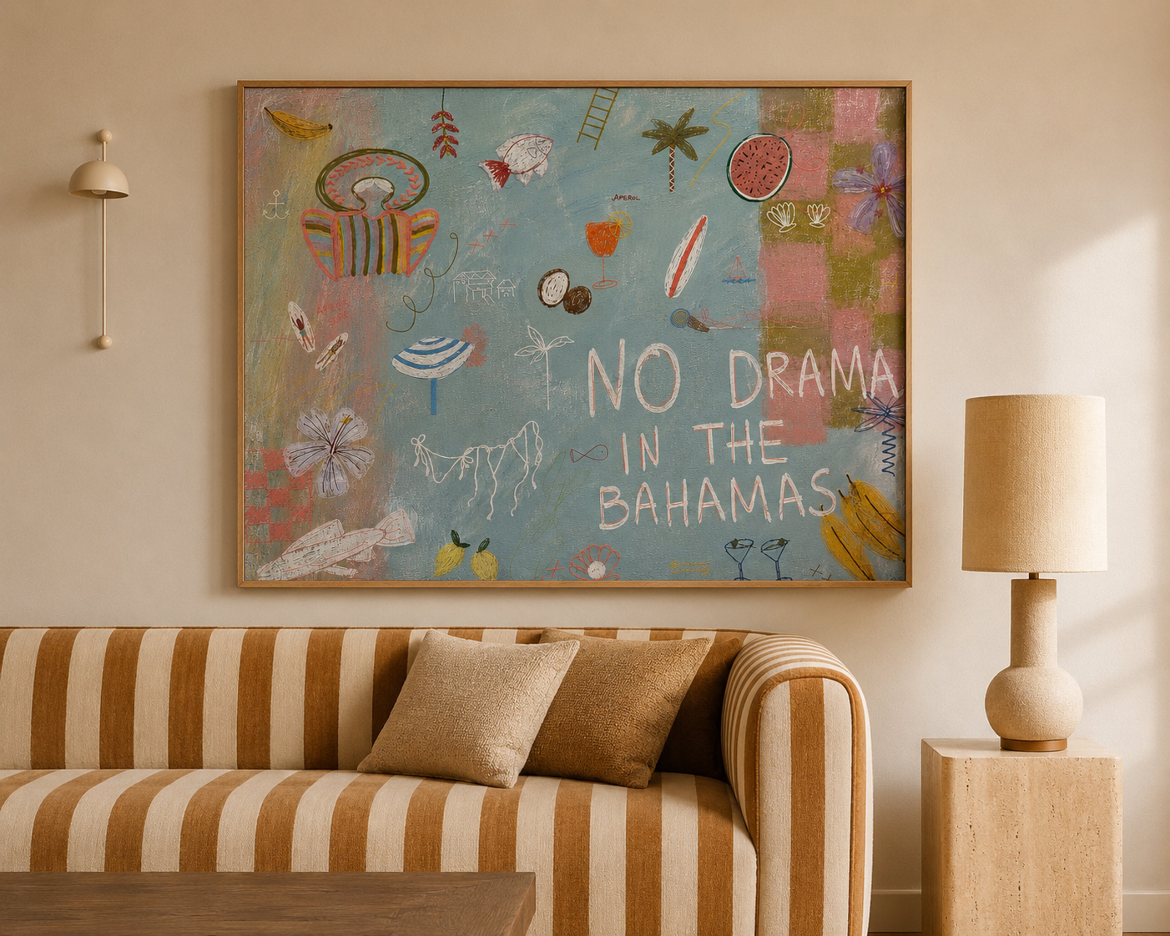 A framed canvas art print featuring a colorful tropical beach illustration and the text 'NO DRAMA IN THE BAHAMAS' hangs on a beige wall above a striped sofa in a styled living room.