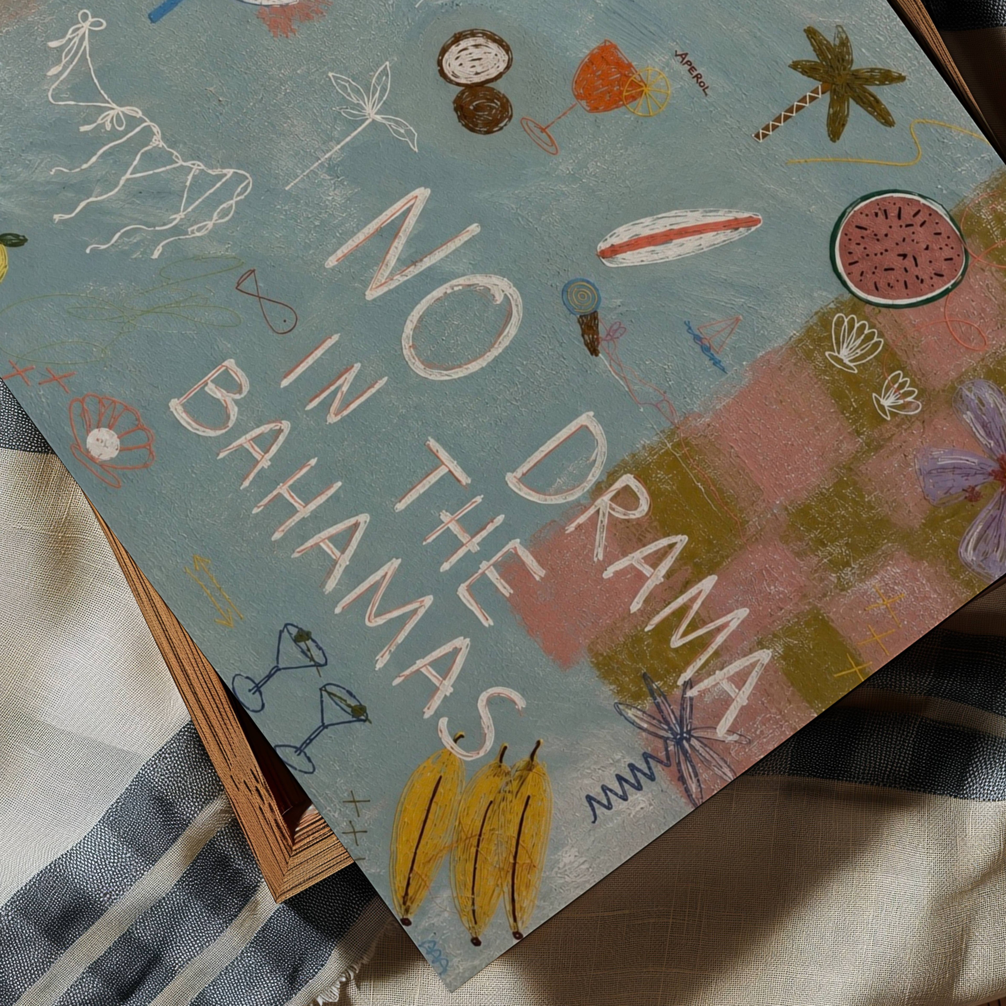 A square art print  featuring the text 'NO DRAMA IN THE BAHAMAS' in large white letters over a painted beach scene. The artwork includes tropical motifs like palm trees, a banana, watermelon, sunglasses, and flowers on a blue-green background, with pink sand and a striped blanket visible underneath.