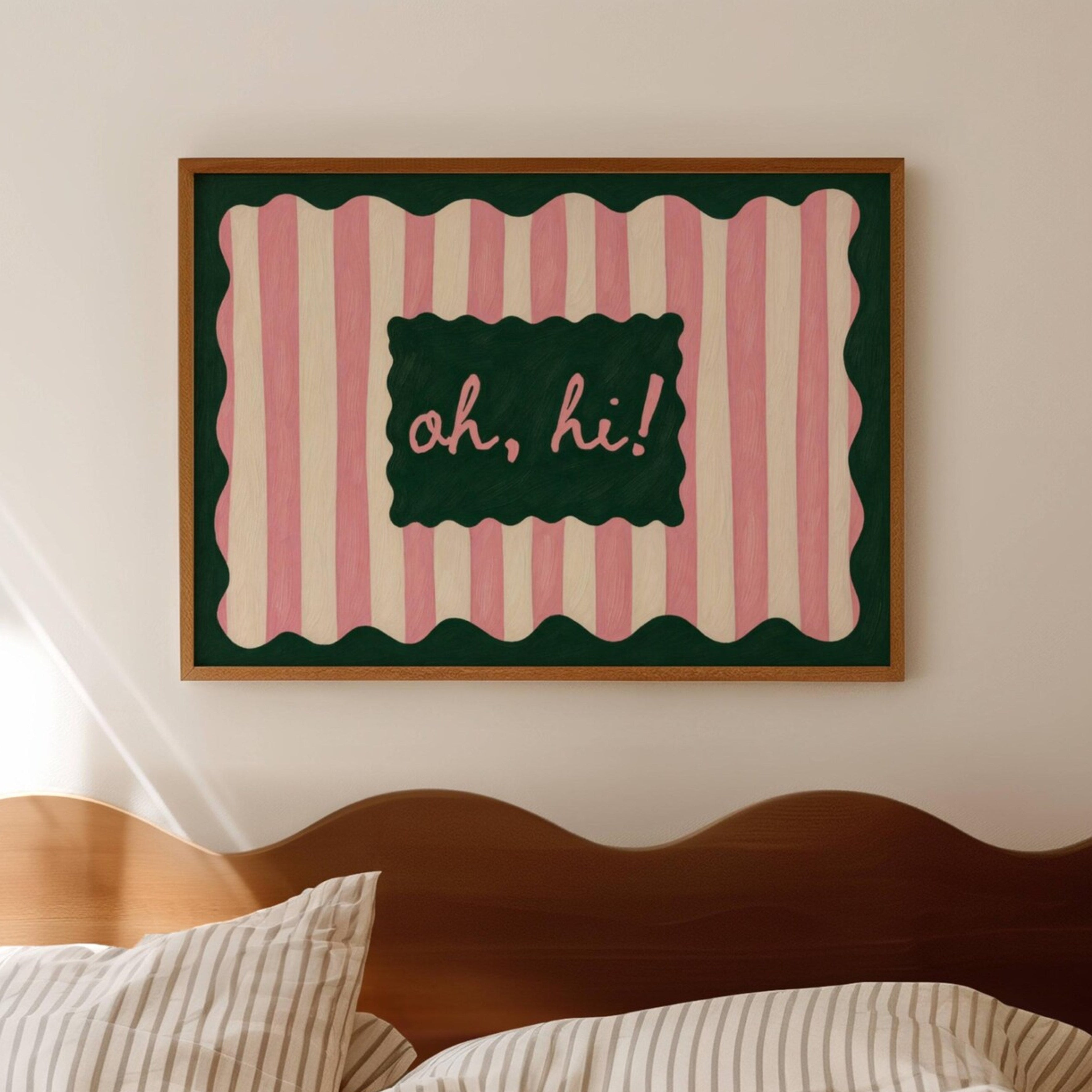 Framed artwork with pink and green striped border and 'oh, hi!' text above a bed.