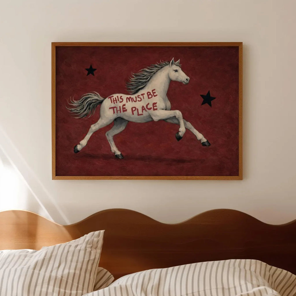 A surreal Symbolic artwork featuring a White Horse running against a rich burgundy background with black stars. The Horse has handwritten quote "This Must Be The Place". This is a hand drawn Contemporary Folk art Print Oil Painting.