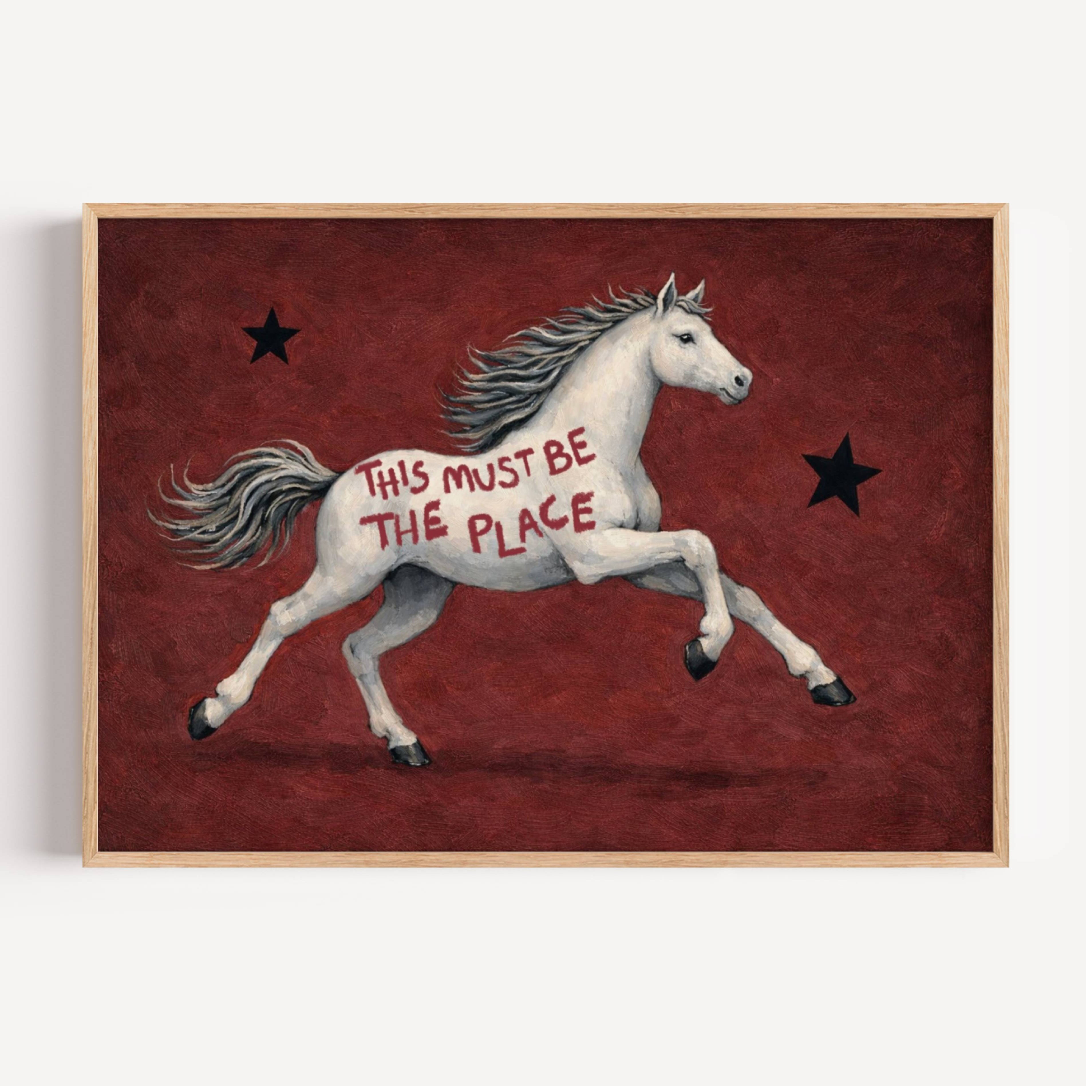 A surreal Symbolic artwork featuring a White Horse running against a rich burgundy background with black stars. The Horse has handwritten quote "This Must Be The Place". This is a hand drawn Contemporary Folk art Print Oil Painting.
