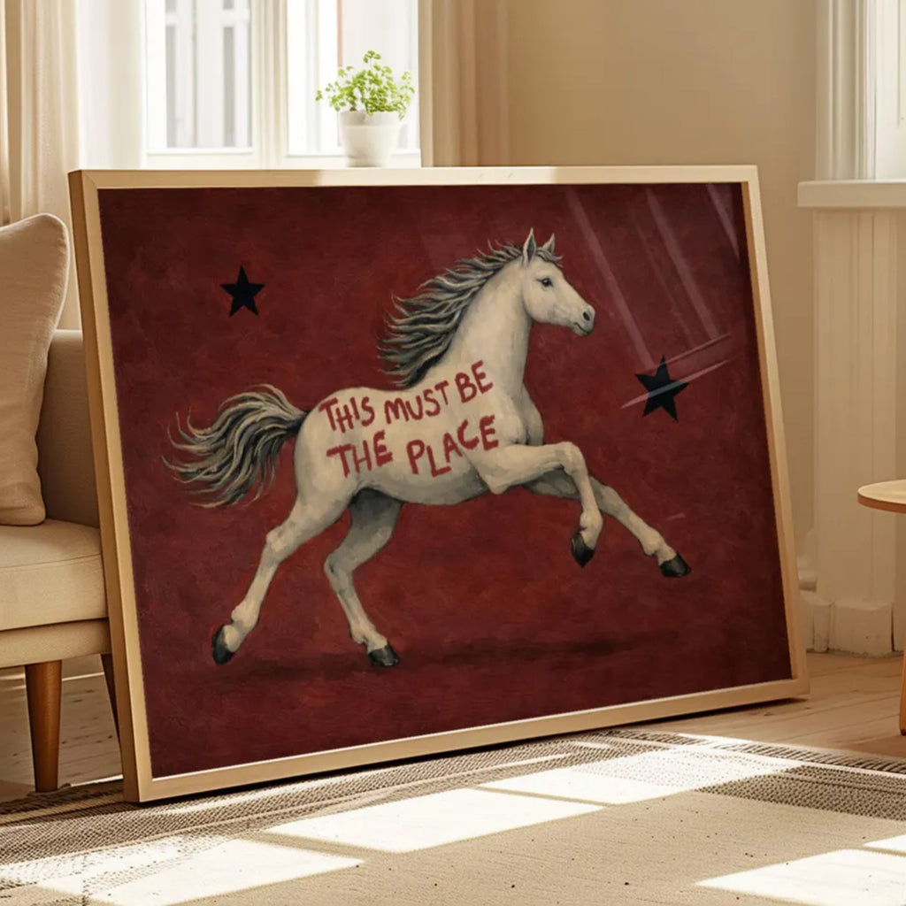 A surreal Symbolic artwork featuring a White Horse running against a rich burgundy background with black stars. The Horse has handwritten quote "This Must Be The Place". This is a hand drawn Contemporary Folk art Print Oil Painting.