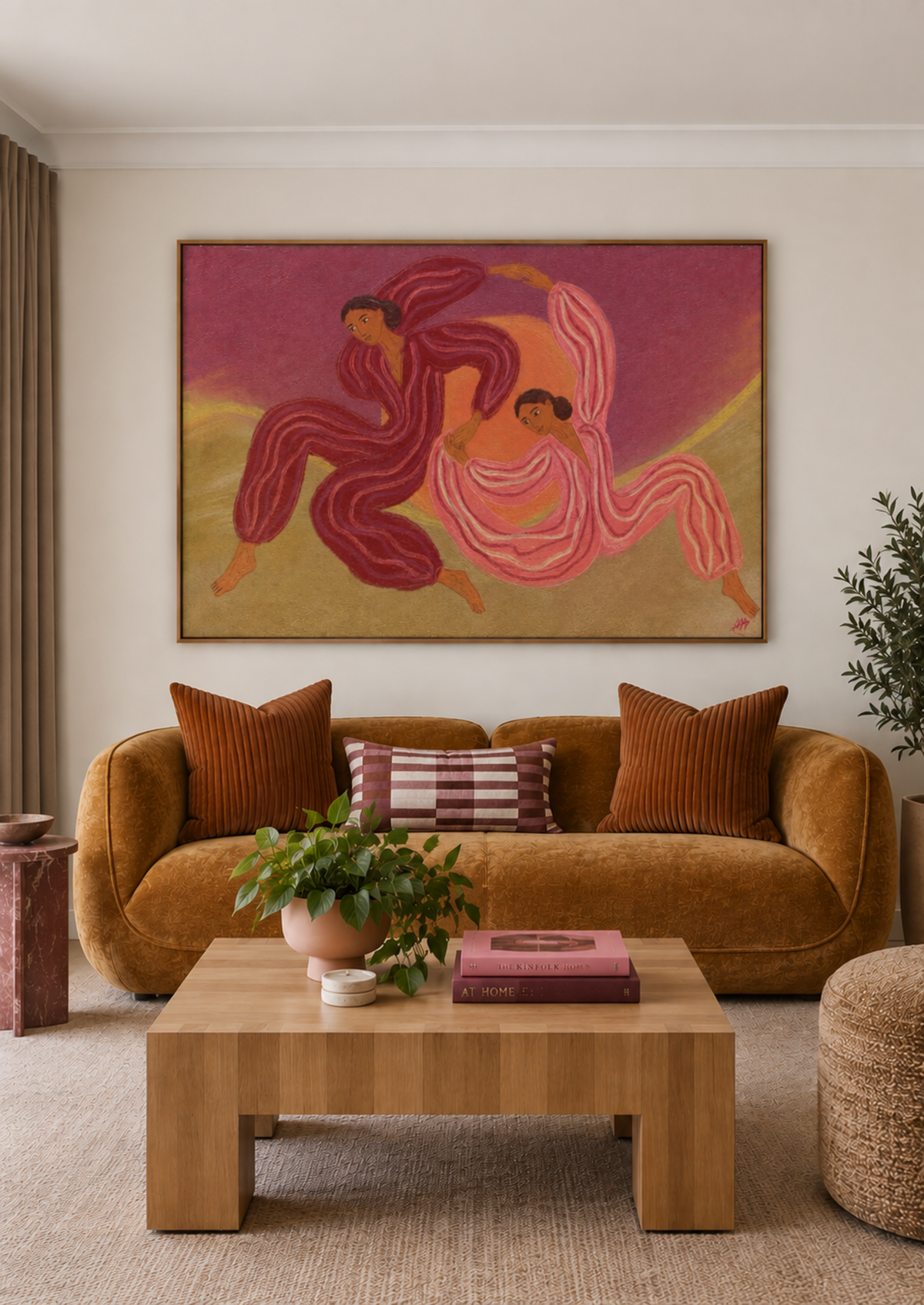 A framed art print depicting two dancing figures in warm pink, red, and gold tones, displayed on a beige wall above a brown velvet sofa in a styled living room.