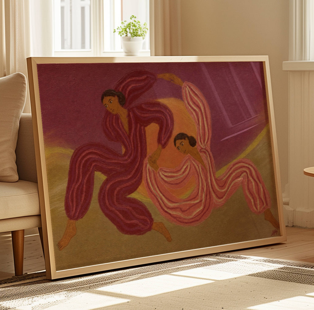 A framed art print depicting two dancing figures in flowing pink, red, and purple garments against a warm beige and gold background, leaning against a sofa in a sunlit living room.
