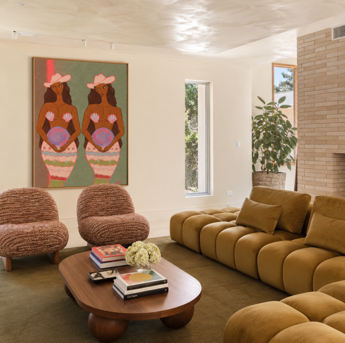 A modern living room featuring a large framed art print of two women in pink hats on the wall, a mustard yellow modular sofa, two textured brown armchairs, and a round wooden coffee table.