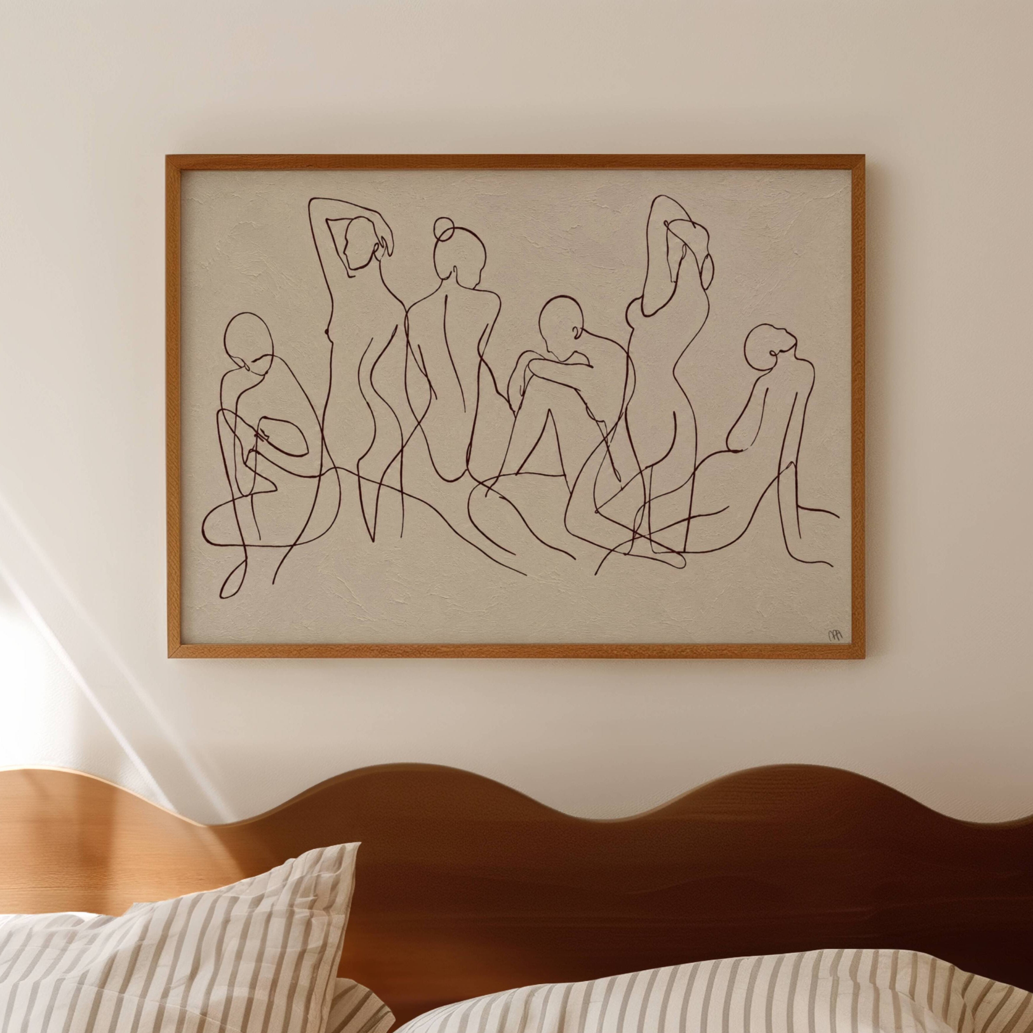 Framed line art of nude figures on a wall above a bed with wooden headboard.