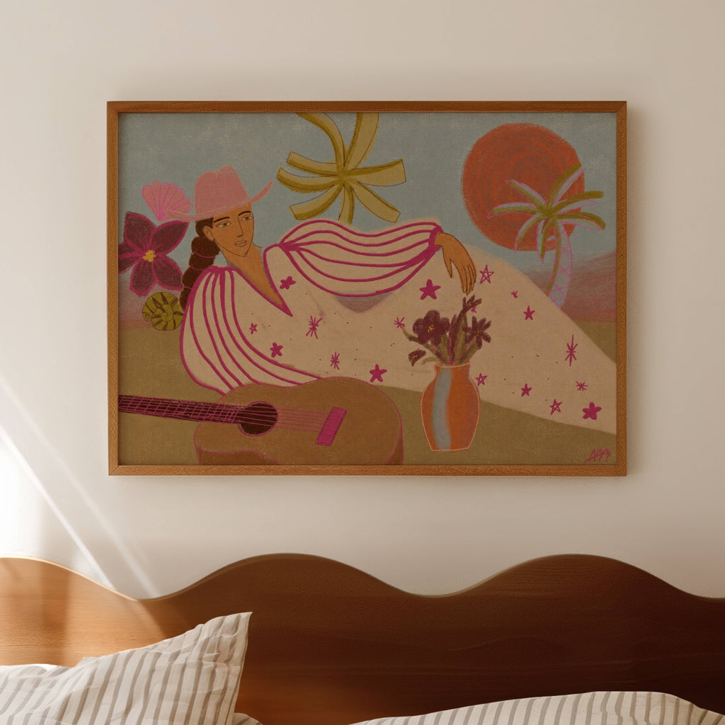 A framed art print featuring a retro-style illustration of a woman in a pink hat and striped dress, reclining with a guitar and flowers, hanging on a beige wall above a wooden headboard.