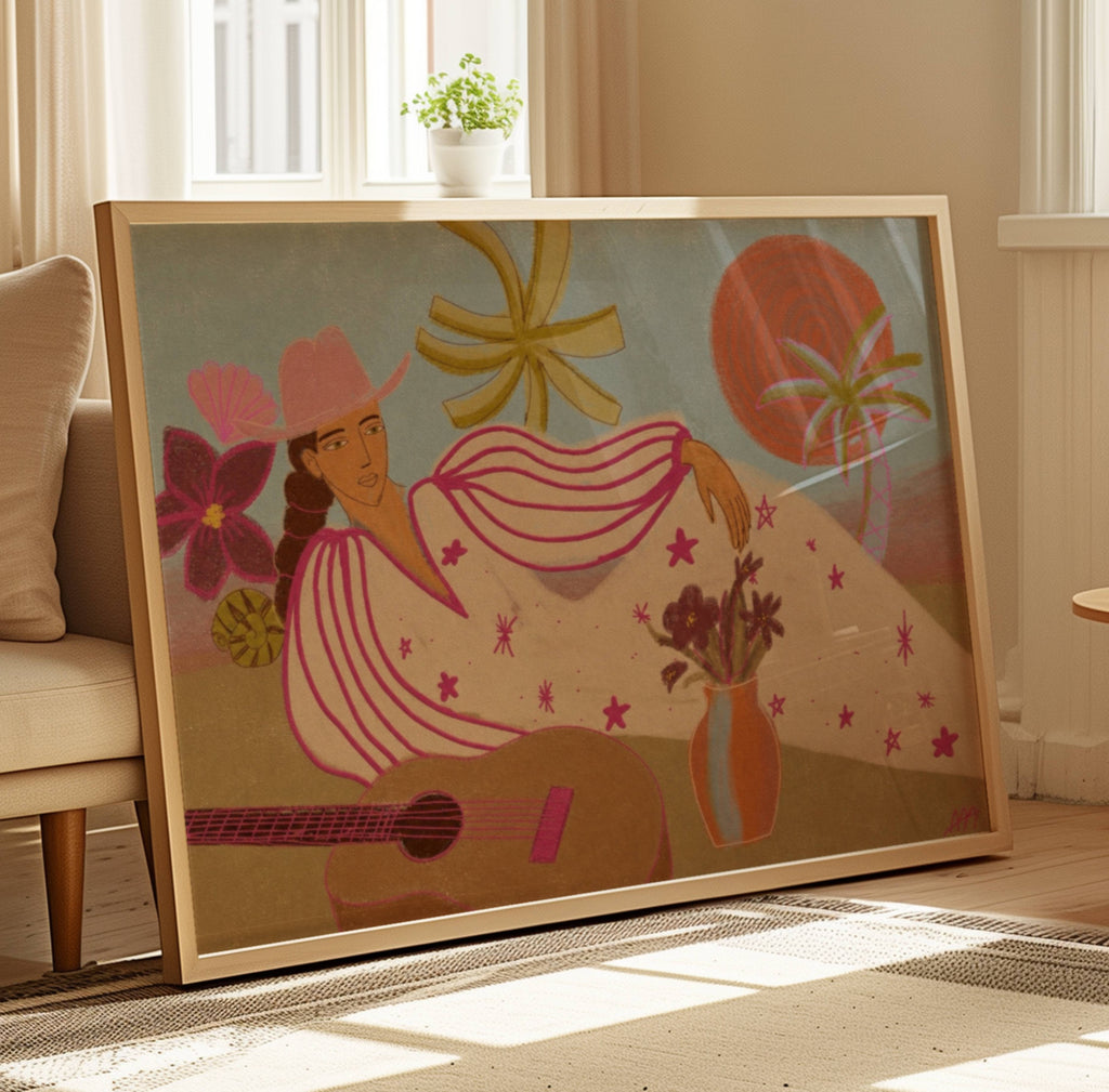 A large framed art print leaning against a beige sofa in a sunlit living room. The artwork features a stylized woman in a pink hat and striped dress with a guitar, flowers, stars, and a vase, set in a warm retro palette.